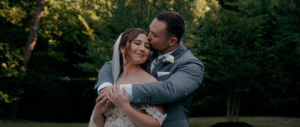 Dallas Wedding Videographer | Adrienne and John | Bethel Rock in Leonard, TX - couple embracing with kiss on the bride's forehead