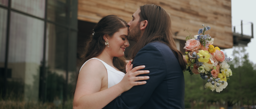 Dallas Wedding Videographer | Dana and Jordan | Watermark Church and HALL Arts Museum Wedding - Groom kissing bride on forehead outside church