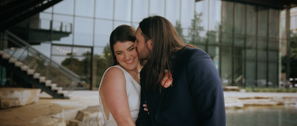 Dallas Wedding Videographer | Dana and Jordan | Watermark Church and HALL Arts Museum Wedding - Bride laughing as Groom kisses cheek