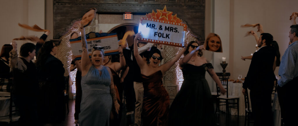 Videography for Wedding Dallas | Houston Wedding Videography | Amanda and Jacob | - bridesmaid's grand entrance holding a "Mr. & Mrs. Folk" sign