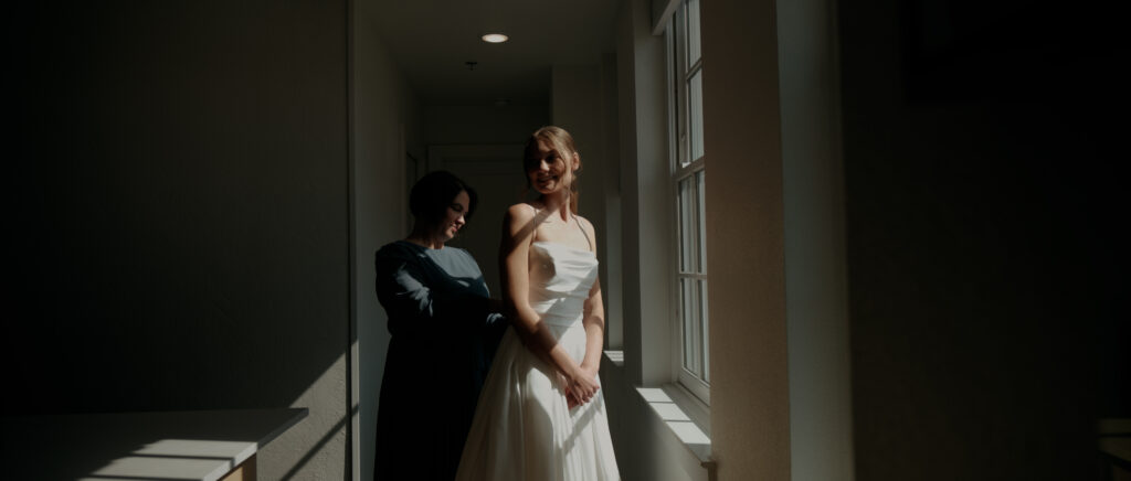 Videography for Wedding Dallas | Tegan and Dayd | - Crazy Water Hotel Wedding Video - Mom buttoning up bride's dress in front of the window
